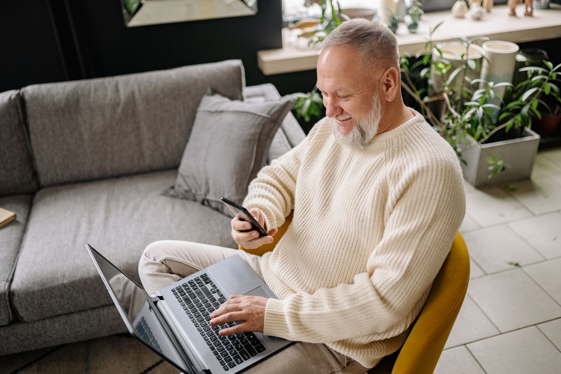 a senior man reading a suspicious email on a laptop with a phone beside him